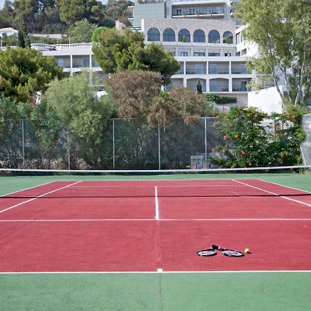 Dolce By Wyndham Athens Attica Riviera Hotel Vravrona Exterior photo The photo shows a tennis court with red and green surfaces. The court is empty, with no players present. In the center, there are a tennis racket and a ball lying on the ground. In the background, there are trees and a building, suggesting the court 