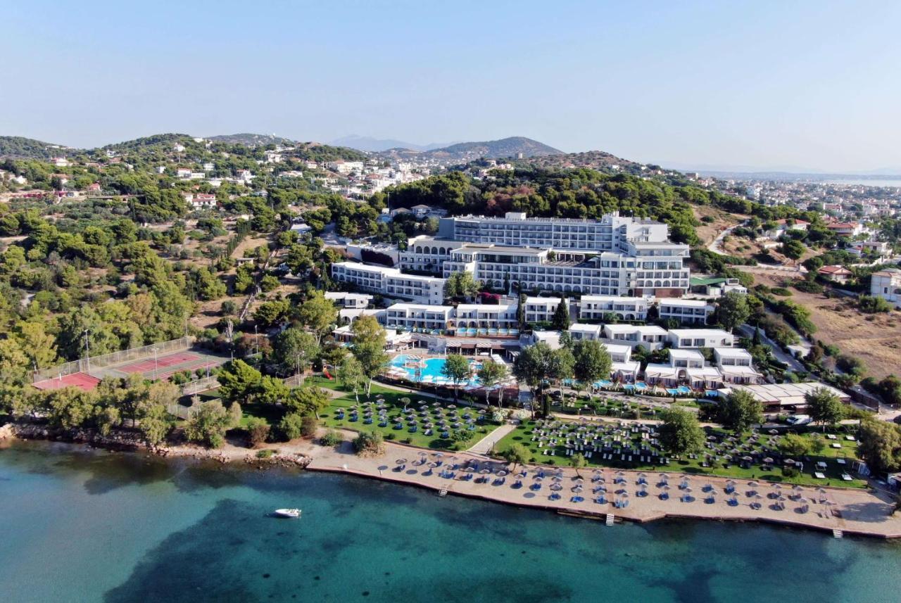 Dolce By Wyndham Athens Attica Riviera Hotel Vravrona Exterior photo The image shows a large hotel complex situated near a beach. It's located on a hillside, surrounded by greenery and trees. The hotel features multiple levels with modern architecture, balconies, and a swimming pool area. In front of the hotel, there'