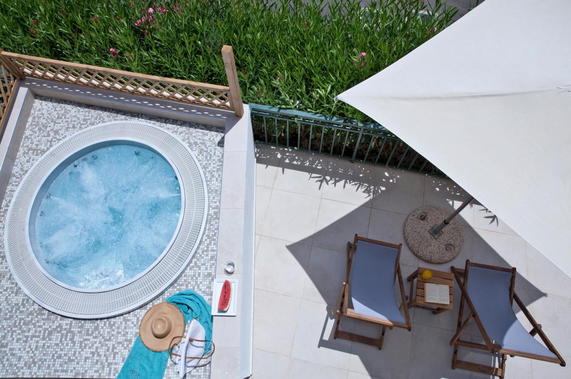 Dolce By Wyndham Athens Attica Riviera Hotel Vravrona Exterior photo The photo shows an overhead view of a relaxing outdoor space. There's a round hot tub with light blue water and a decorative edge. Nearby, a couple of wooden lounge chairs are positioned underneath a large umbrella to provide shade. A small side tabl