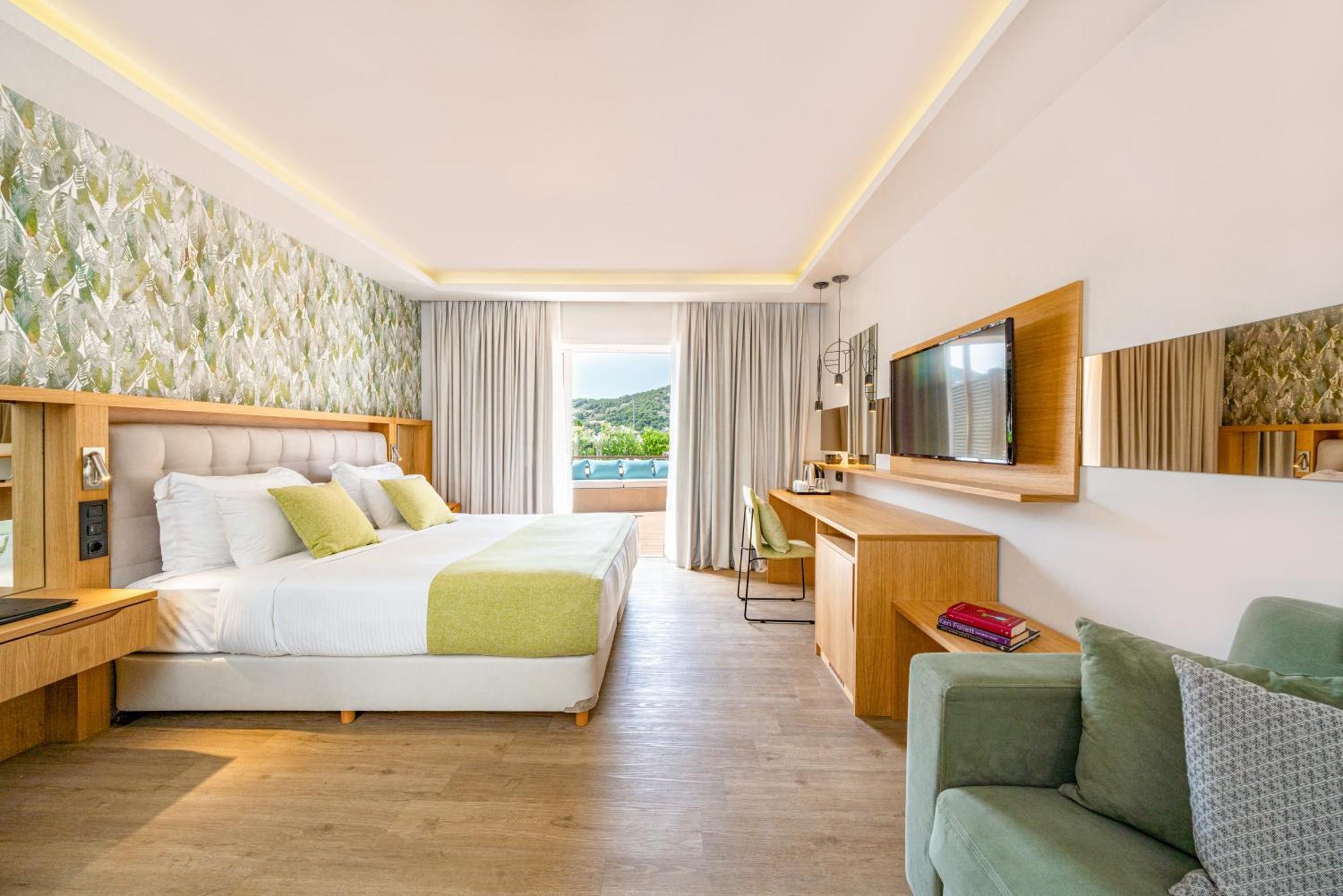 Dolce By Wyndham Athens Attica Riviera Hotel Vravrona Exterior photo The photo shows a modern hotel room featuring a large bed with white linens and accent pillows in light green. Behind the bed is a decorative wall with floral patterns. On one side of the room, there is a comfortable chair and a small side table. Acr